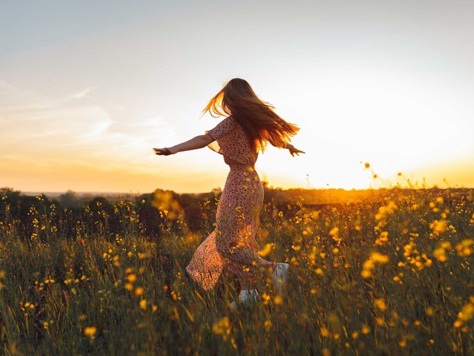 Frau tanzt auf einer Blumenwiese im Sommer | © Getty Images/Olga Rolenko