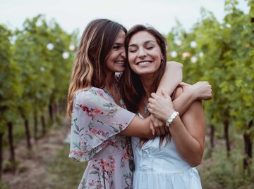 Zwei Schwestern umarmen sich in der Natur und lachen. | © Getty Images/Westend61