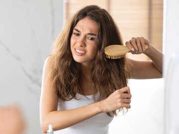 Junge Frau kämmt sich frustriert die Haare | © Getty Images/Prostock-Studio