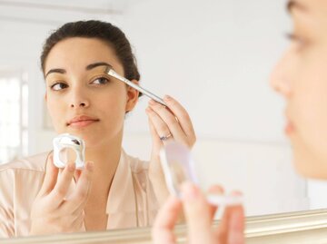 Frau schminkt Augen im Spiegel | © Getty Images/Christopher Robbins
