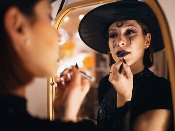 Frau schminkt sich für Halloween vor Spiegel | © Getty Images/SrdjanPav