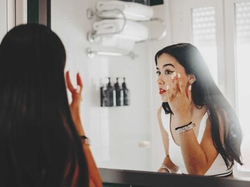 Junge Frau schminkt sich vor dem Spiegel | © Getty Images/Carol Yepes