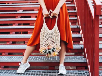 Frau in rotem Kleid trägt eine Einkaufstasche | © Getty Images/Olena Ruban