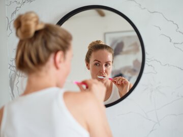 Frau putzt sich vor einem Spiegel die Zähne | © Getty Images/Sergey Mironov