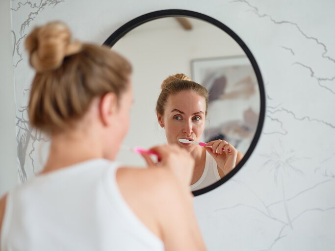 Frau putzt sich vor einem Spiegel die Zähne | © Getty Images/Sergey Mironov