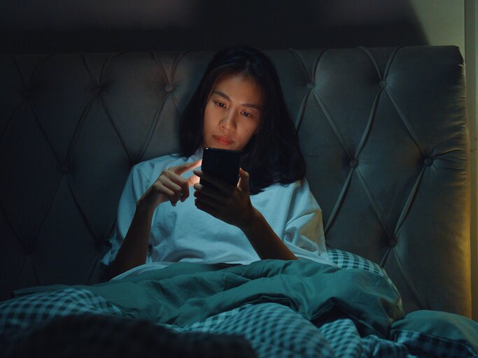 Eine junge Frau ist spät abends noch am Handy | © GettyImages/MTStock Studio