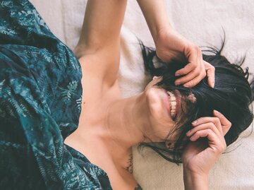 Frau liegt im Bett und lacht | © Getty Images