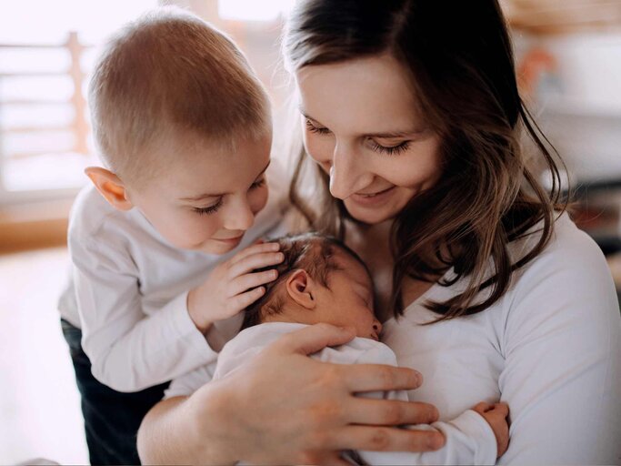 Junge Mutter mit neugeborenem Baby und älterem Geschwisterkind | © Getty Images/Halfpoint Images
