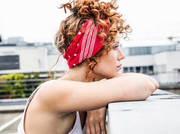 Frau mit roten Locken und einem Bandana in den Haaren schaut traurig in die Ferne. | © Getty Images / Westend61