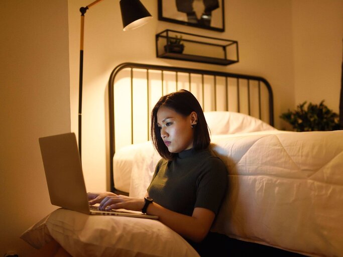 Person sitzt vor Bett am Boden mit Laptop | © Getty Images/Carlina Teteris