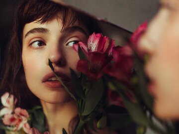 Frau mit Blumen blickt in den Spiegel | © Getty Images/Igor Ustynskyy