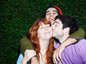 Eine Frau und zwei Männer umarmen und küssen sich | © Getty Images/Tara Moore