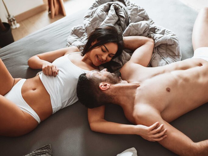 Paar liegt gemeinsam im Bett und lächelt sich an | © Getty Images/AleksandarGeorgiev