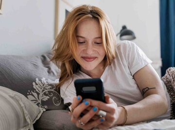 Junge Frau schreibt etwas mit ihrem Smartphone und lächelt dabei | © Getty Images/Willie B. Thomas