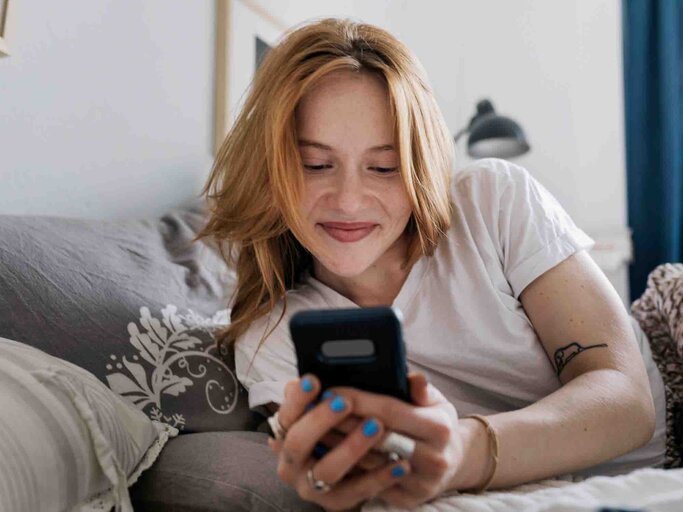 Junge Frau schreibt etwas mit ihrem Smartphone und lächelt dabei | © Getty Images/Willie B. Thomas