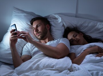 Mann ist an seinem Handy während seine Partnerin schläft | © Getty Images/AndreyPopov