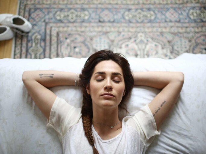 Frau mit geschlossenen Augen auf dem Bett liegend | © Getty Images/Catherine Delahaye