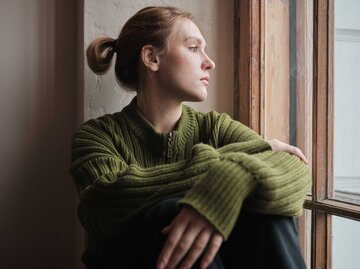 Nachdenkliche junge Frau schaut aus dem Fenster | © Getty Images/MementoJpeg