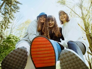 Drei junge Frauen halten ihre Schuhsohlen in die Kamera. | © Getty Images/Tatsiana Volkava