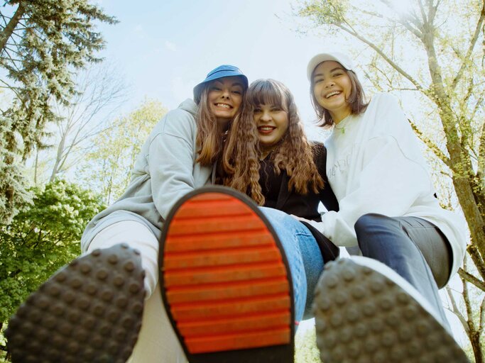 Drei junge Frauen halten ihre Schuhsohlen in die Kamera. | © Getty Images/Tatsiana Volkava
