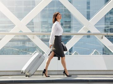 Geschäftsfrau läuft mit einem Koffer durch den Flughafen. | © Adobe Stock/mimagephotos