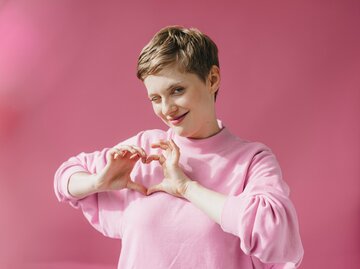 Portrait einer jungen Frau mit pastellfarbenem Pullover. Sie formt mit ihren Händen ein Herz. | © Getty Images/Westend61