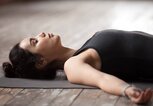 Frau meditiert im Liegen auf einer Yogamatte | © iStock | fizkes