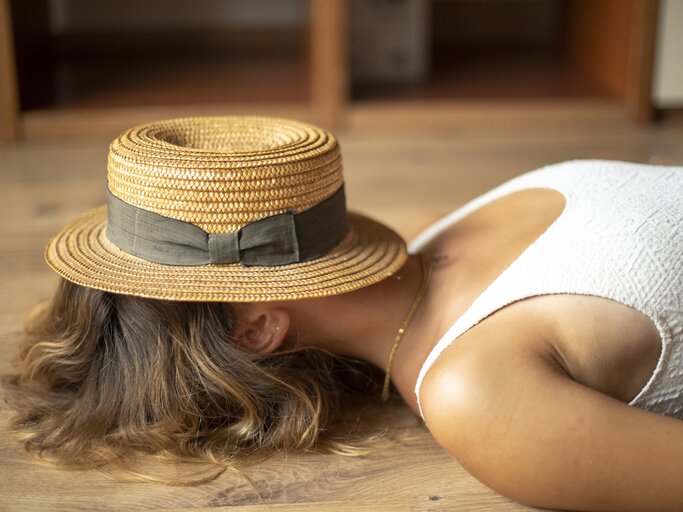 Frau liegt mit Sonnenhut auf dem Kopf am Boden | © Getty Images/	Westend61