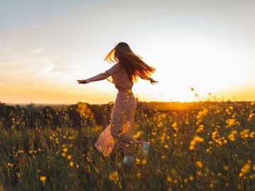 Frau tanzt im sommerlichen Blumenfeld | © GettyImages/Olga Rolenko