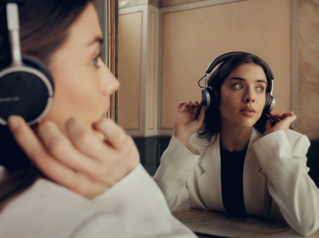 Frau mit weißem Blazer sitzt vor einem Spiegel und trägt beyerdynamic On-Ear-Kopfhörer. | © beyerdynamic
