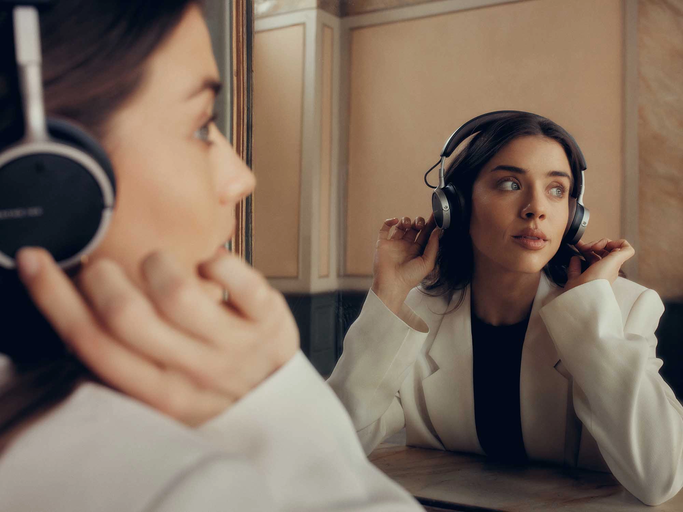 Frau mit weißem Blazer sitzt vor einem Spiegel und trägt beyerdynamic On-Ear-Kopfhörer. | © beyerdynamic