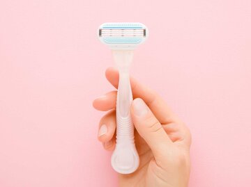 Ein Damenrasierer wird vor einen rosa Hintergrund gehalten | © Adobe Stock/fotoduets