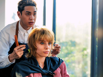 Friseur schneidet Kundin die Haare im Salon – beide wirken konzentriert und entspannt beim Haarschnitt | © Getty Images/Nitat Termmee