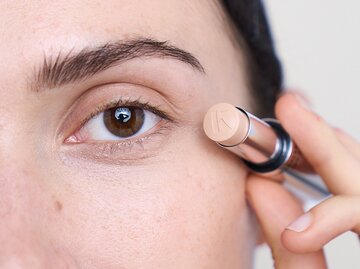 Dunkelhaarige Frau hält Concealer von kess ans Gesicht | © PR