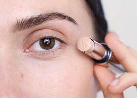 Dunkelhaarige Frau hält Concealer von kess ans Gesicht