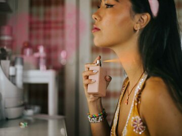 Frau sprüht sich vor dem Spiegel Parfum auf den Hals. | © GettyImages/Carol Yepes