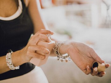 Nahaufnahme: Frau mit hellem Nagellack trägt Parfum auf, Schmuckarmbänder glänzen dezent im warmen Tageslicht. | © Getty Images/Carol Yepes