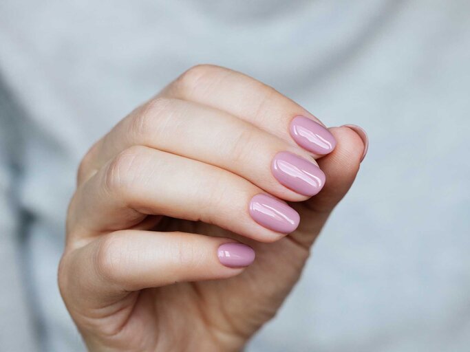 Die Hand einer Frau trägt kurze Gelnägel mit einem hellen Rosa. | © GettyImages/Mariia Demchenko