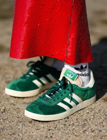Eine Frau trägt grüne Adidas Gazelle mit einem roten Paillettenrock.  | © Getty Images/Edward Berthelot