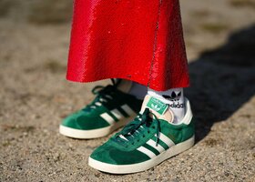 Eine Frau trägt grüne Adidas Gazelle mit einem roten Paillettenrock. 