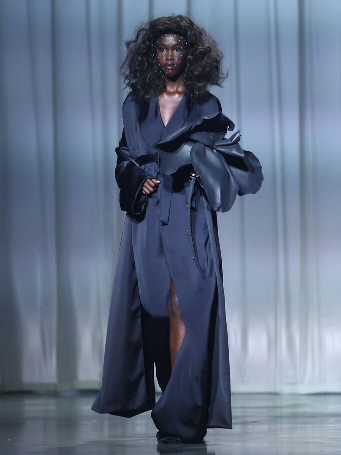 Model in schwarzem Mantel mit schwarzer Blume auf dem Laufsteg von Kilian Kerner | © Getty Images/Joern Pollex