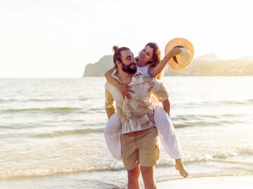 Mann und Frau am Strand. Er trägt sie Huckepack | © Getty Images/KALA STUDIO