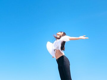 Glückliche Frau, die frische Luft atmet, die Arme in die Höhe hebt und einen sonnigen blauem Himmel genießt | © Adobe Stock/max_play