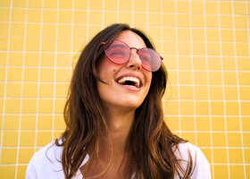 Brünette mit Sonnenbrille auf lacht und blickt nach oben