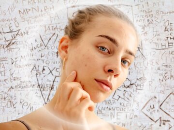 Junge Frau betrachtet ihre Haut und berührt ihr Kinn – Symbolbild für Selbstkritik und die Sympathie, die durch Unvollkommenheit entsteht. | © Getty Images/Maksym Belchenko