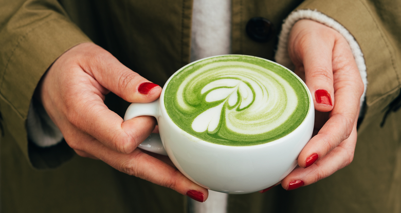 Frau mit roten Nägeln hält Tasse mit Matcha Latte in den Händen | © Getty Images/Anastasiia Voloshko