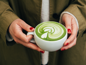 Frau mit roten Nägeln hält Tasse mit Matcha Latte in den Händen | © Getty Images/Anastasiia Voloshko