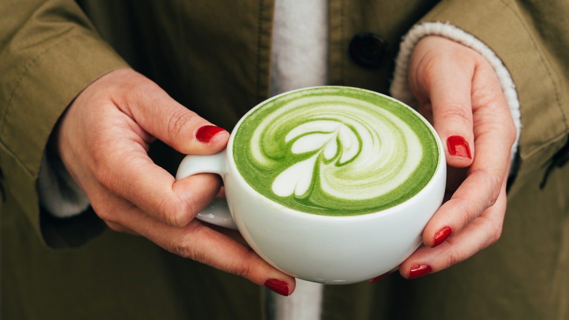 Frau mit roten Nägeln hält Tasse mit Matcha Latte in den Händen | © Getty Images/Anastasiia Voloshko