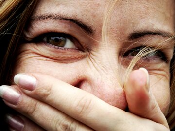 Glückliche Frau mit Lachfalten hält sich die Hand vor den Mund. | © GettyImages/	photo by giorgio raffaelli