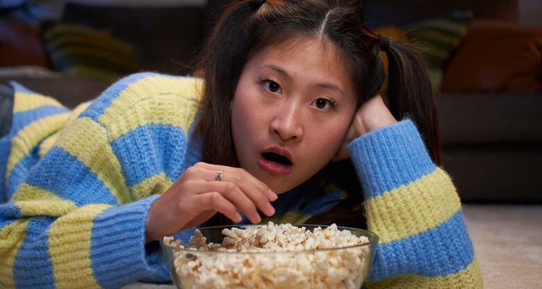 Junge Frau schaut einen Film und isst Popcorn. | © Getty Images/Carlos Barquero